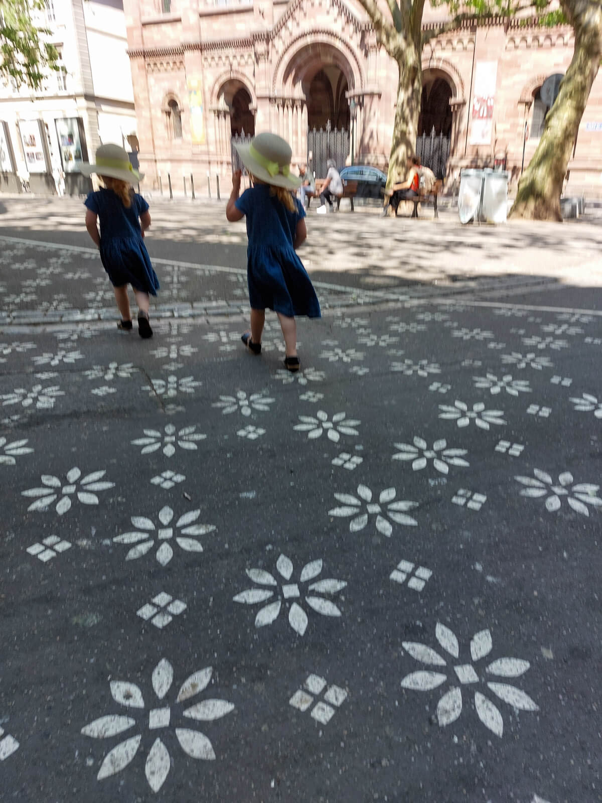 justyourtime-mamacoaching Zwei Kinder im Sommerkleid und Sonnenhut laufen spielerisch durch eine Stadt – Symbol für Leichtigkeit, Selbstwahrnehmung und Balance im MamaCoaching.